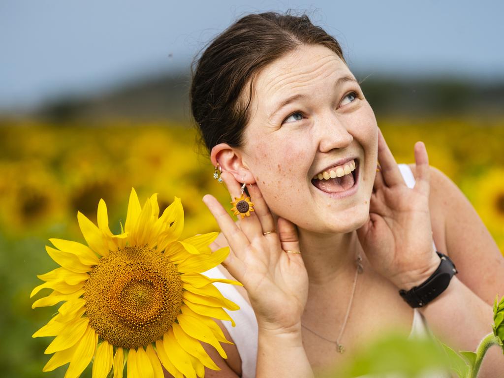 Laura Hoek shows off her sunflower earrings while standing in the Warraba Sunflowers summer crop, Wednesday, January 4, 2023.