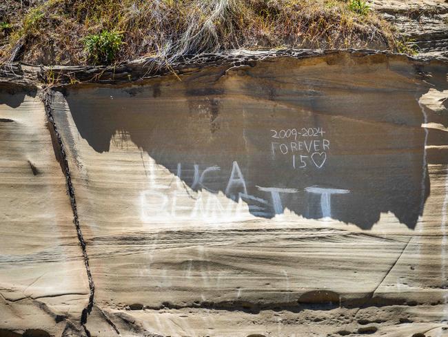 Friends of Luca Bennett scratch his name into the rock at North Avoca where he was swept off yesterday afternoon. Picture: Tom Parrish