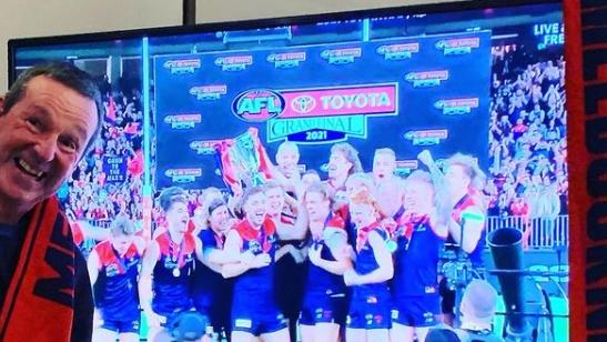 Neale Daniher sitting next to his TV as the Daemons collect the 2021 AFL Premiership cup.  CAPTION on the Instagram post: "Back of the bus baby! All Melbourne supporters rejoice"