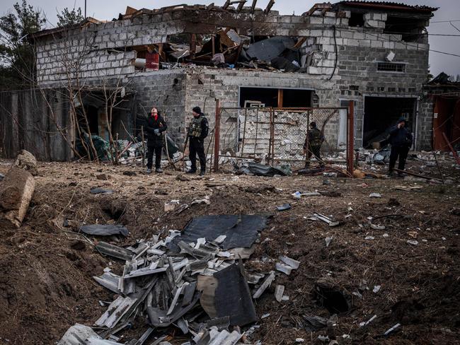 Police officers and residents stand next to a shell crater in front of a house damaged by shelling, on the outskirts Kyiv. Picture: AFP