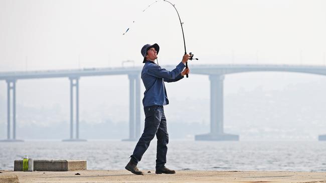 Liam Ostapowicz, 20, of Lenah Valley, went fishing along the River Derwent as smoke from the bushfires made its way to Hobart. Picture: ZAK SIMMONDS