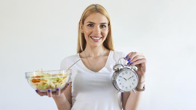 Young woman holding clock and Healthy food of salad Intermittent fasting concept. Time to lose weight , eating control or time to diet concept.