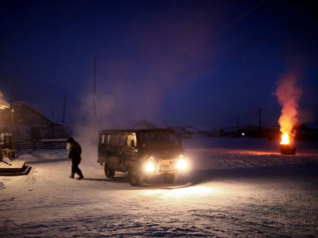 A man leaves his van and walks into Oymyakon's only shop as paper waste is burnt in a 40 gallon drum.