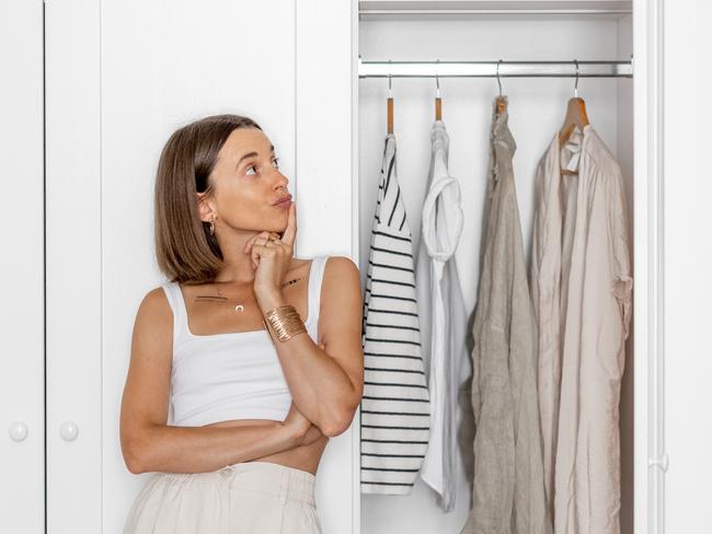 Young woman chooses what to wear, standing near the white closet at home. Concept of choice problem, style and fashion