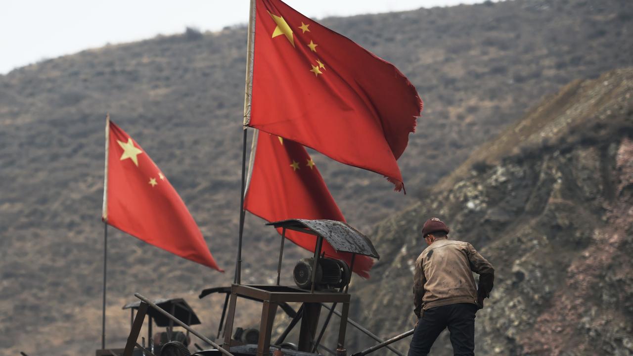 Chinese flags next to a worker clearing a conveyor belt used to transport coal. Picture: AFP