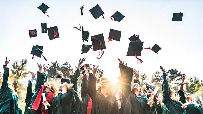 Large group of students celebrating their graduation day outdoors while throwing their caps up in the air.