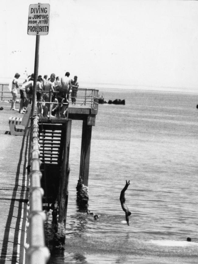 A warning sign at Glenelg, prohibiting diving or jumping from the jetty. A group of boys defy the ban and jump into the water November 28, 1989.