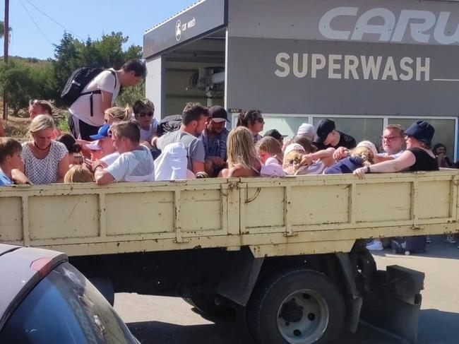 Tourists sit in the back of an open air lorry as they are evacuated during wildfires on the Greek island of Rhodes on July 22, 2023. More than 2,000 people were ferried to safety from beaches on the Greek island of Rhodes on July 22, 2023, where a wildfire has been raging out of control for five days. Three coastguard boats were leading more than 30 private vessels in the emergency evacuation, while a Greek navy boat was heading to the area. (Photo by AFP stringer / Eurokinissi / AFP)