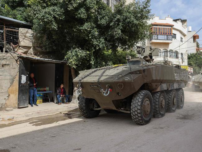 Palestinian shopkeepers look as Israeli armoured vehicles drive by during a raid in the eastern neighbourhood of Jenin. Picture: AFP