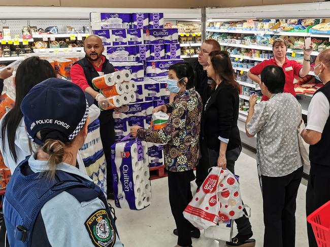 People receiving toilet paper, paper towel and pasta as a Police Officer watches on at Coles Supermarket, Epping in Sydney, Friday, March 20, 2020. Supermarkets have been struggling to keep up with demand for products such as toilet paper in recent days, as panic buying as a result of the Covid-19 pandemic has resulted in people purchasing far more than usual. Supermarkets have put in place limits on the quantity people can purchase of many everyday items. (AAP Image/James Gourley) NO ARCHIVING