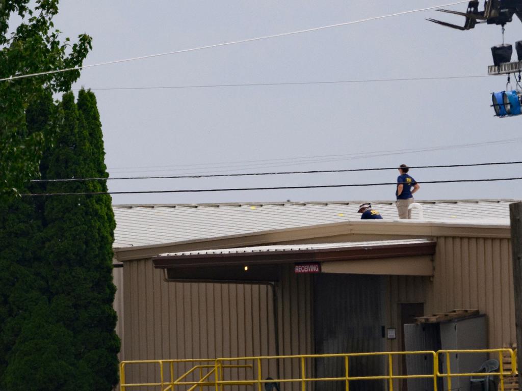 Two FBI investigators scan the roof of AGR International, despite the dangers of its sloped roof. Picture: AFP