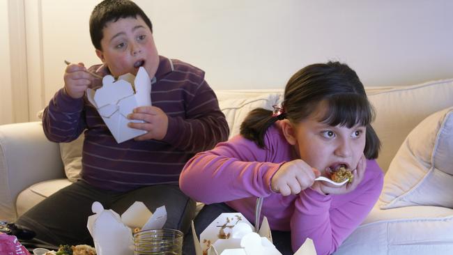 Overweight Brother and Sister Sitting Side by Side on a Sofa Eating Takeaway Food and Watching the TV