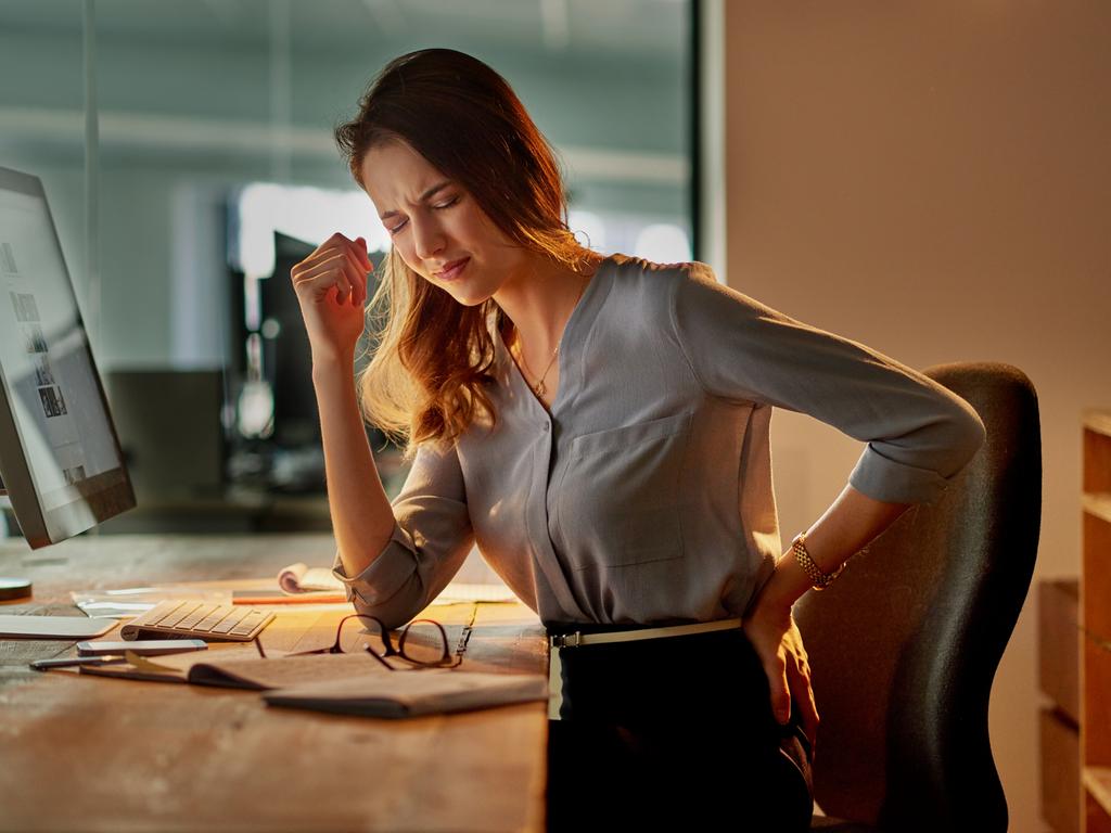 Shot of an attractive young businesswoman holding her back in pain while working late in the office