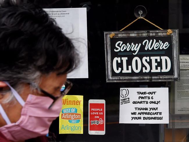 (FILES) In this file photo taken on May 5, 2020 a woman wearing a face mask walks past a sign in the window of a food store announcing that the business is closed during a shelter in place lockdown order during an outbreak of COVID-19 coronavirus in Arlington, Virginia. - The coronavirus arrived in the US early this year, followed by deaths, business shutdowns and layoffs, rendering a previously healthy economy unrecognizable. Data from the government and private surveys has shown that the economic damage is deep and may take years to recover from, but on Friday, a new Labor Department survey is expected to show unemployment spiking, perhaps to as high as 20 percent, a number few living Americans have ever seen before. Ahead of the report's release, AFP spoke to three people about how the virus has changed the course of their lives in the world's largest economy. (Photo by Olivier DOULIERY / AFP)