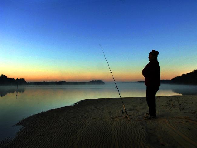 A fisherman waits in the morning light on the banks of the Macleay River, at Fishermans Reach.