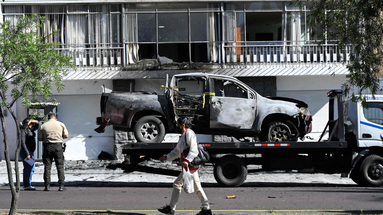 A woman passes by a burned car in front of the headquarters of the agency in charge of managing prisons (SNAI) on August 31, 2023 in Quito. Picture: Rodrigo BUENDIA / AFP