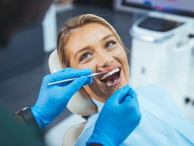 Dentist and patient in dentist office. Over the shoulder view of a dentist examining a patients teeth in dental clinic. Female having her teeth examined by a dentist.