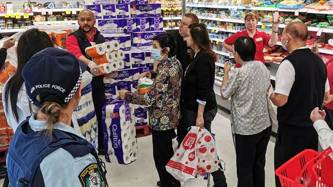 People receiving toilet paper, paper towel and pasta as a Police Officer watches on at Coles Supermarket, Epping in Sydney, Friday, March 20, 2020. Supermarkets have been struggling to keep up with demand for products such as toilet paper in recent days, as panic buying as a result of the Covid-19 pandemic has resulted in people purchasing far more than usual. Supermarkets have put in place limits on the quantity people can purchase of many everyday items. (AAP Image/James Gourley) NO ARCHIVING