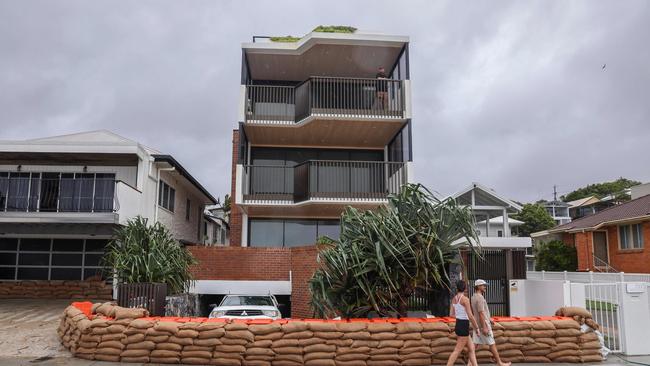 People walk past a block of units surrounded by sand bags to protect it from the storm surge of large waves generated by Tropical Cyclone Alfred at Currumbin on the Gold Coast on March 6, 2025. The outer fringe of Tropical Cyclone Alfred started whipping eastern Australia on March 6, bringing drenching rains and record-breaking waves to a heavily populated region rarely hit by typhoons. (Photo by David GRAY / AFP)