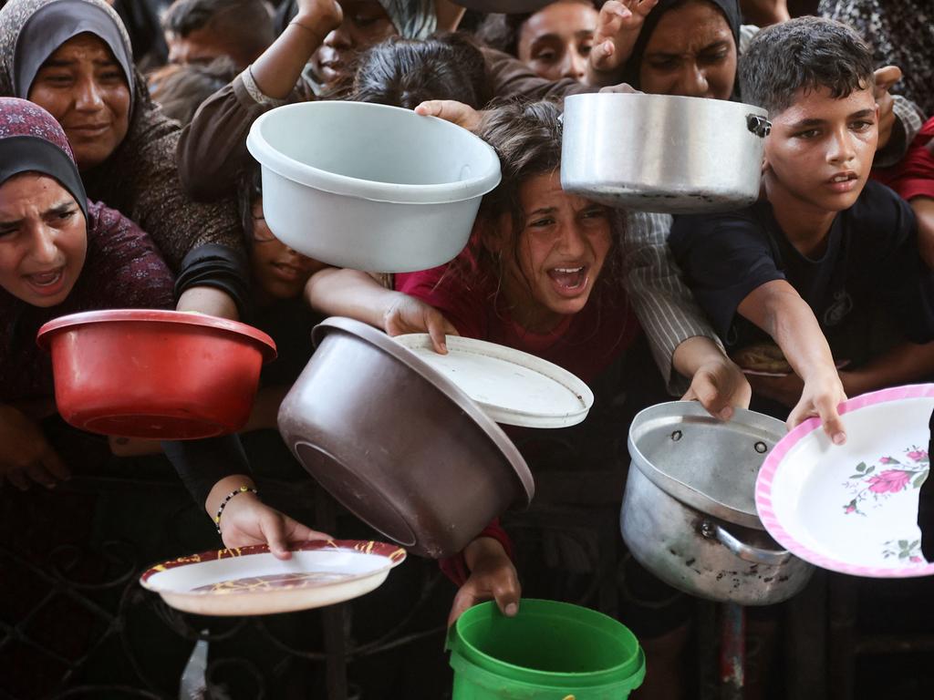 Palestinians, mostly children, hold out their plates toward a man, to receive their share of vegetable patties prepared by volunteers in Beit Lahia in the northern Gaza Strip. Picture: AFP