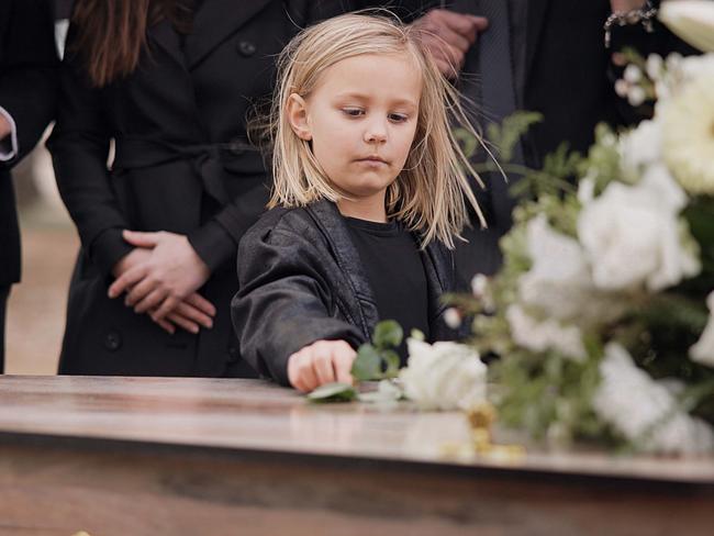 Death, grief and girl at funeral with flower on coffin, family and sad child at service in graveyard for respect. Roses, loss and people at wood casket in cemetery with kid crying at grave for burial