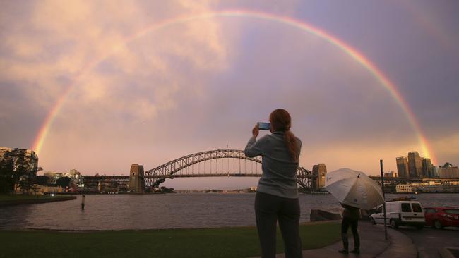 A woman takes a photograph as a rainbow forms over the Harbour Bridge yesterday.