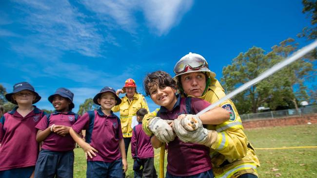 Halfway Creek RFS visit Coffs Primary School. Birhad Kenjo hold the hose with the help of support teacher and volunteer firefighter Joanne Conway with captain Tony Wade in the background.