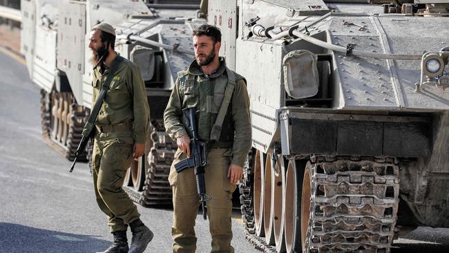 Israeli army soldiers walk before tracked vehicles deployed at a position in the Upper Galilee region in northern Israel near the border with southern Lebanon.