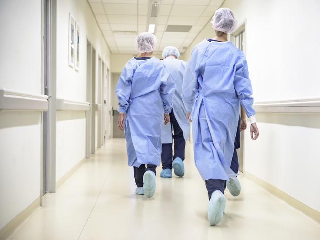 Rear view of male and female surgical team wearing gowns, caps, shoe covers, and walking down hospital corridor to operating room.