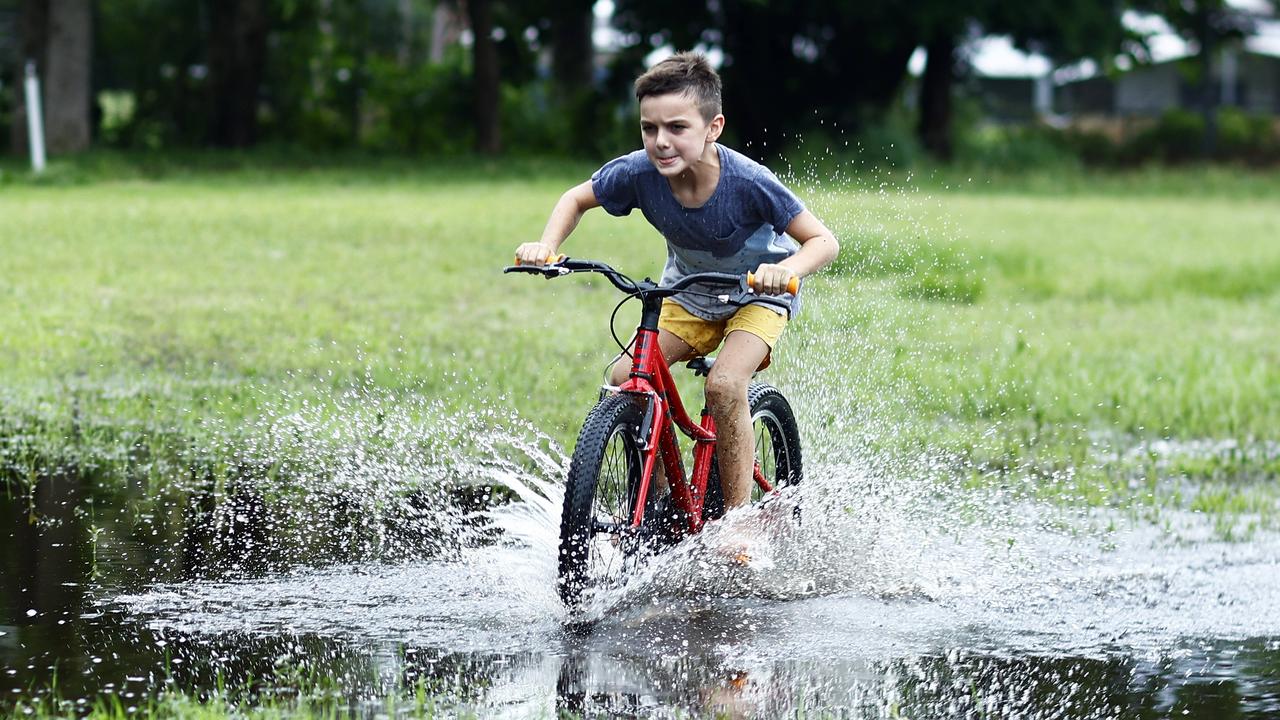 Hunter Cairns, 9, rides his new bicycle through large puddles caused by heavy rain fall at Holloways Beach. Picture: Brendan Radke