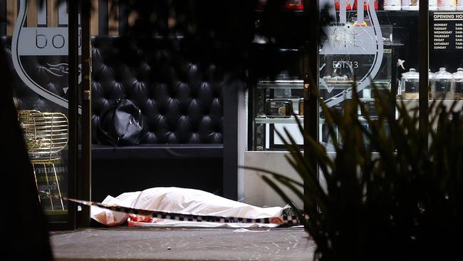 The body of Omar Zahed lies covered by a white blanket in the foyer with a bullet hole in the glass door next to him. Picture: Toby Zerna / Daily Telegraph