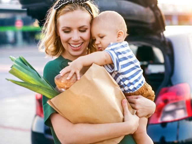 Beautiful young mother with her little baby son in front of a supermarket, holding paper shopping bag. Woman with a boy standing by the car.Istock image for wellbeing in Gold Coast Eye