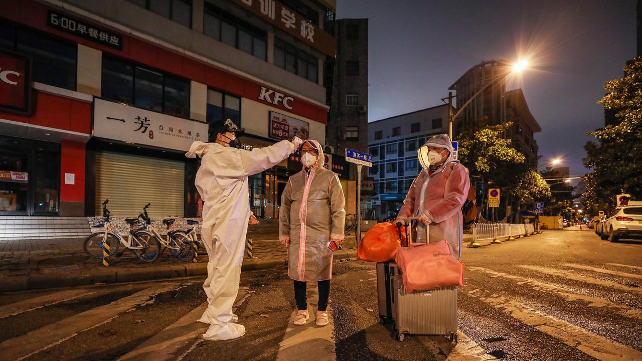 A volunteer (L) checks the body temperature of two people outside a hospital in Wuhan. Picture: STR / AFP