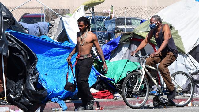 A man wearing a mask cycles past tents housing the homeless lining a street in Los Angeles. Picture: Frederic J. Brown/AFP