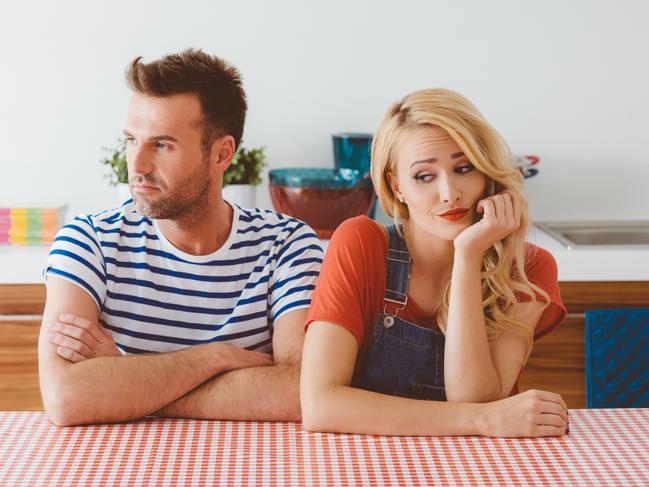 Adult couple sitting at the table in the kitchen at home, not speaking.