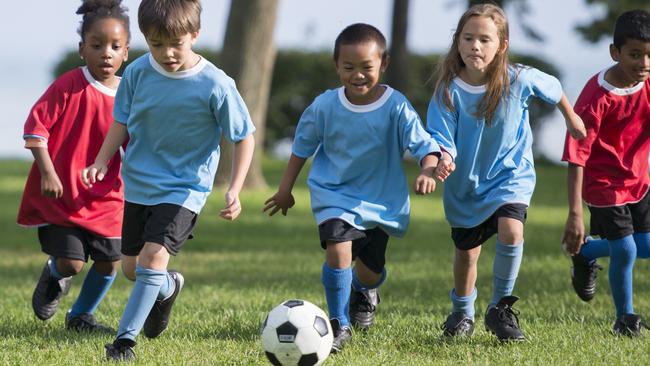 A multi-ethnic group of elementary age children are playing a soccer game outside on a sunny day at the park.
