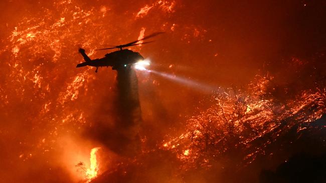 A firefighting helicopter drops water as the Palisades fire grows near the Mandeville Canyon neighbourhood and Encino. Picture: AFP