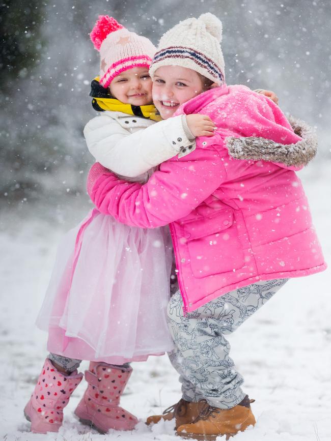 Grace, six, keeps her little sister Sage Wareham, four, warm as the snow falls. Picture: Sarah Matray