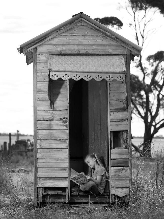 A girl reads in an old outdoor dunny.