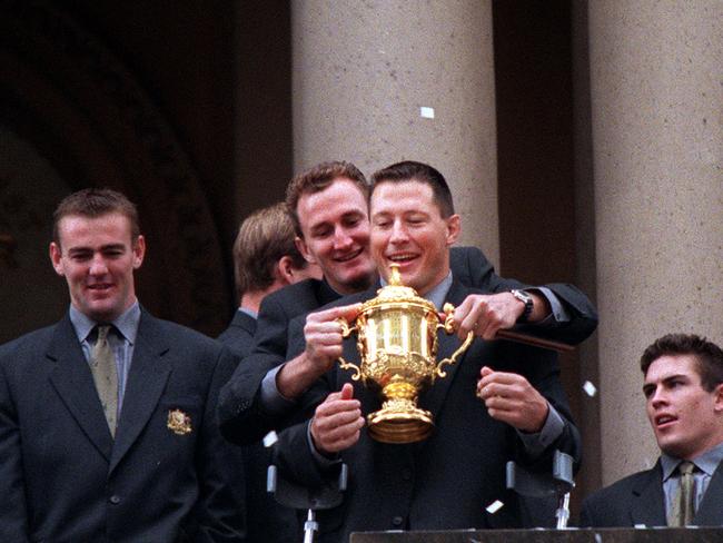 Injured Wallabies player Phil Kearns and teammates with William Webb Ellis aka Bill trophy on balcony of Sydney Town Hall following tickertape parade celebrating Australia's victory in 1999 World Cup final. Picture: Grant Turner