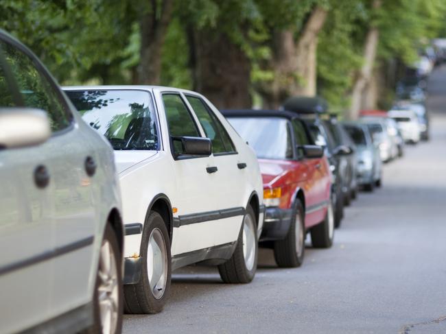 Street with long row of cars parked along a tree avenue.