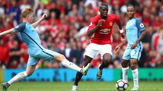 Paul Pogba of Manchester United (C) takes the ball past Kevin De Bruyne of Manchester City