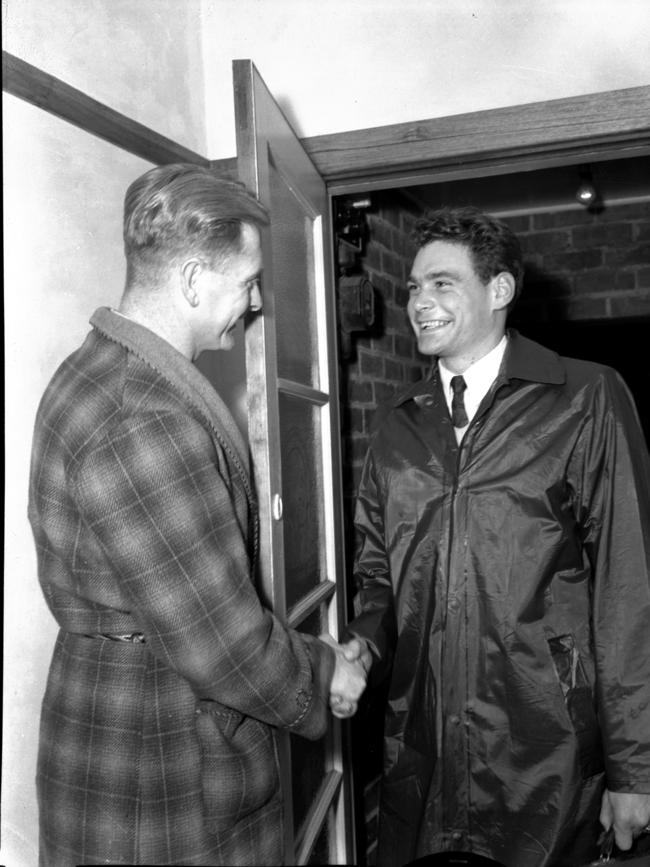 Barassi, wearing a raincoat, being met at the front door by Norm Smith wearing a dressing-gown.