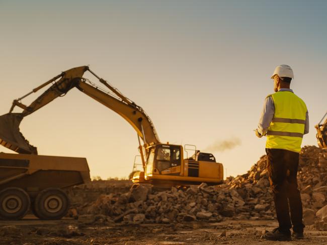 Man Inspecting Building Progress. Excavator Loading Materials Into Industrial Truck