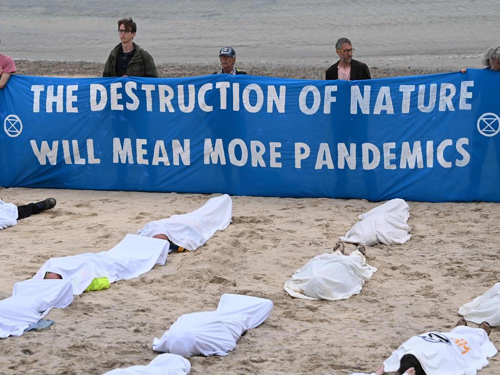 Activists hold a banner reading 'The destruction of nature will lead to more pandemics' as others pose as dead bodies during a climate change protest by Extinction Rebellion on the beach in St Ives, Cornwall.