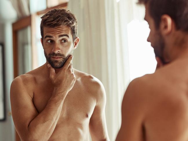 Shot of a shirtless man checking out his skin in the bathroom mirror