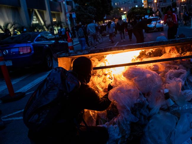 A straggling demonstrator lights a dumpster on fire after police disperse a largely peaceful crowd outside City Hall in San Francisco, California. Picture: AFP