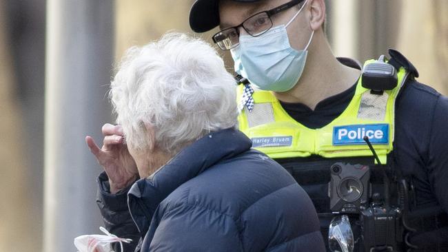 A police officer helps an elderly woman put on a face mask in the Melbourne CBD. Picture: NCA NewsWire / David Geraghty