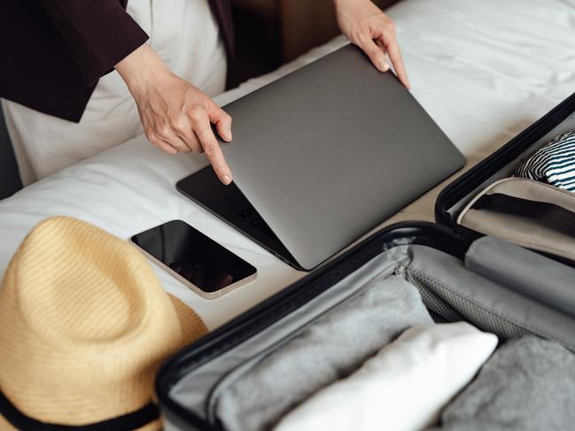 7 sophisticated suitcase essentials. Picture: Getty Images Female hands closing laptop, packaging clothing into the suitcase in hotel room on a business trip. Bleisure travel. Work life balance.