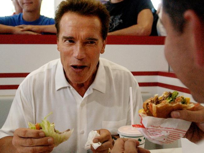 Arnold Schwarzenegger, left, eats a hamburger wrapped in lettuce during a lunch break at an In-N-Out restaurant in California. Picture: Stephen Savoia/AP